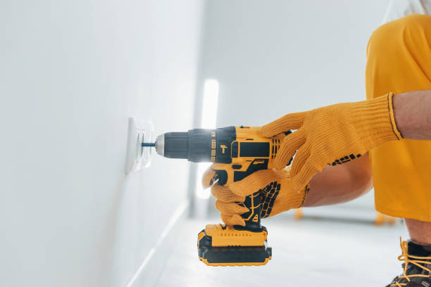 istock Handyman in yellow uniform works with electricity and installing new socket by using automatic screwdriver. House renovation conception 1324858557