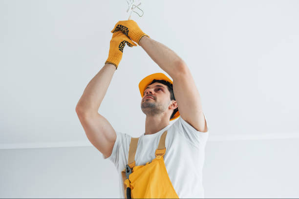 istock Handyman in yellow uniform changing light bulb. House renovation conception 1324858578