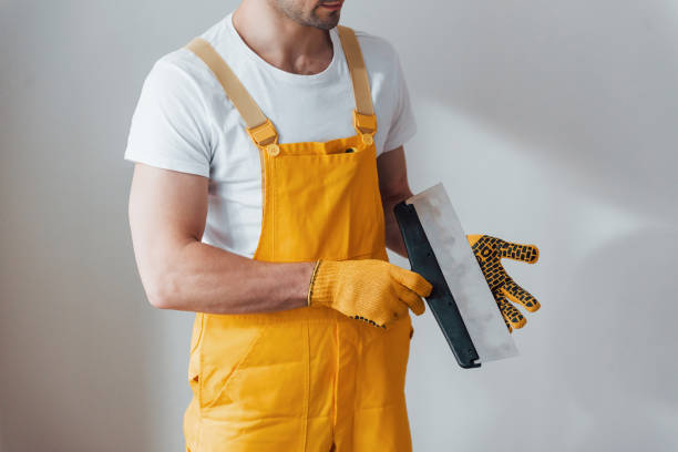istock Handyman in yellow uniform standing against white wall. House renovation conception 1324858704