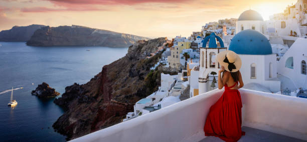 kobieta turystyczna w czerwonej sukience i kapeluszu siedzi na balkonie w miejscowości oia, santorini - hat oia europe vacations zdjęcia i obrazy z banku zdjęć