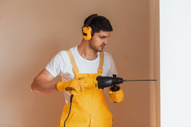 istock Handyman in yellow uniform works indoors by using hammer drill. House renovation conception 1324860225