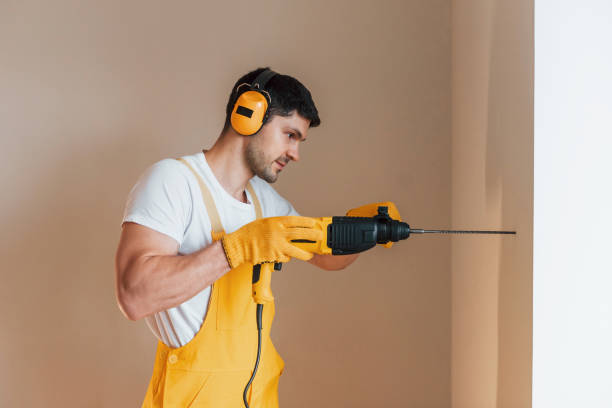 istock Handyman in yellow uniform works indoors by using hammer drill. House renovation conception 1324860241
