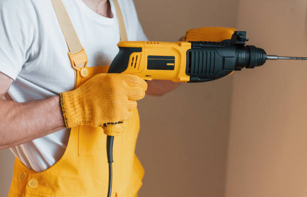 istock Handyman in yellow uniform works indoors by using hammer drill. House renovation conception 1324860290