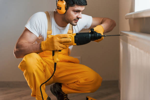 istock Handyman in yellow uniform works indoors by using hammer drill. House renovation conception 1324860363