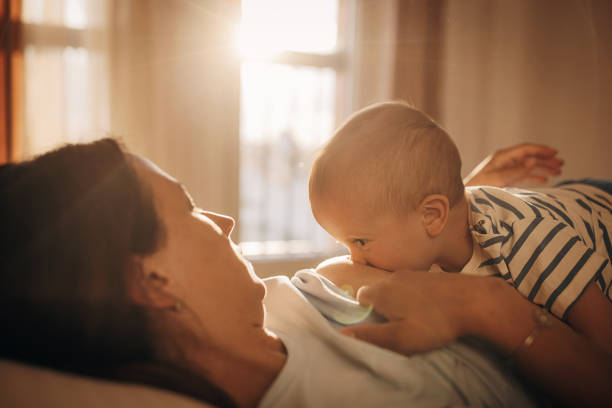 Two people, mother breastfeeding her baby boy son in bedroom at home.
