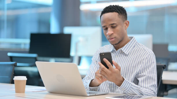 istock African Businessman with Laptop using Smartphone at Work 1324865035