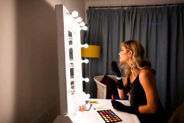 istock Side view beautiful young woman applying make up at mirror with lights 1324865562