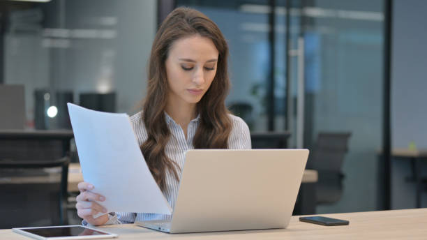 istock Young Businesswoman With Laptop Reading Documents at Work 1324865574