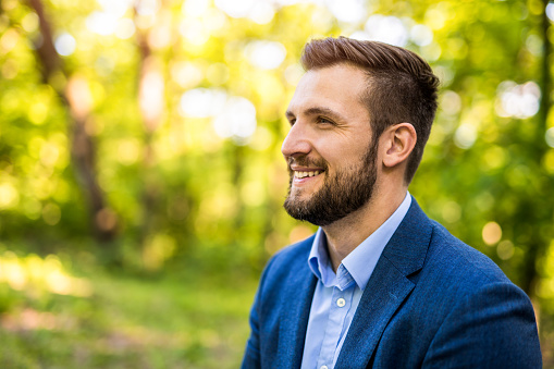 Young smiling businessman catching inspiration in nature. He is taking a break from work and city.