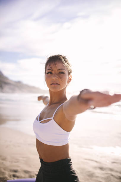 Woman performing yoga in warrior pose Woman performing yoga in warrior pose, Virabhadrasana. Fit woman stretching her arms at the beach. warrior 2 stock pictures, royalty-free photos & images