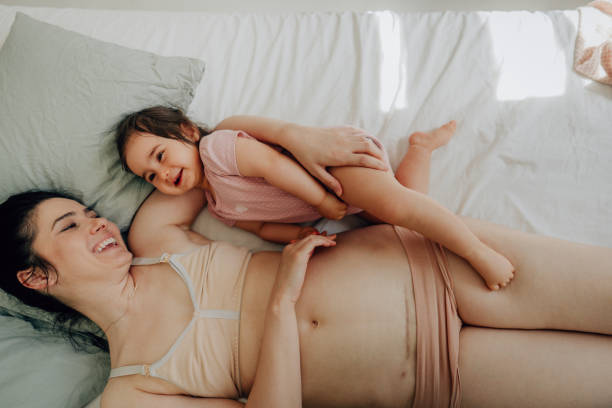 Mother with c-section scar and her baby lying on the bed Photo of mother with c-section scar on a belly and her baby lying on the bed 8 months pregnant stock pictures, royalty-free photos & images