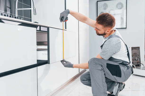 istock Young professional plumber in grey uniform measuring table by using meter on the kitchen 1324872540