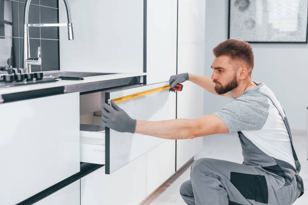 istock Young professional plumber in grey uniform measuring table by using meter on the kitchen 1324872549