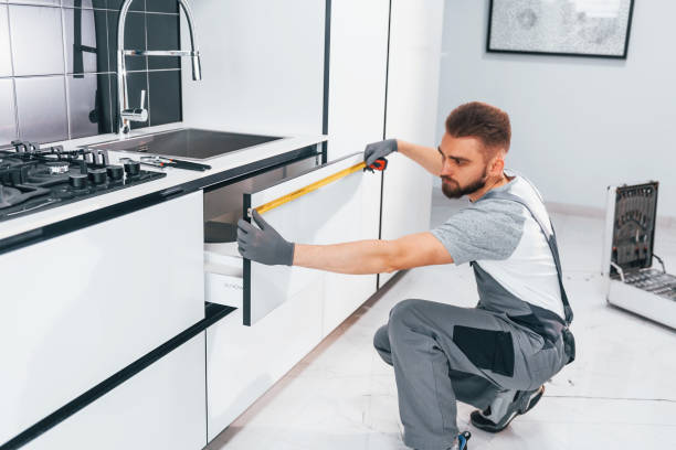 istock Young professional plumber in grey uniform measuring table by using meter on the kitchen 1324872580