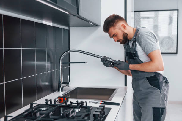 istock Young professional plumber in grey uniform fixing water tap on the kitchen 1324872611