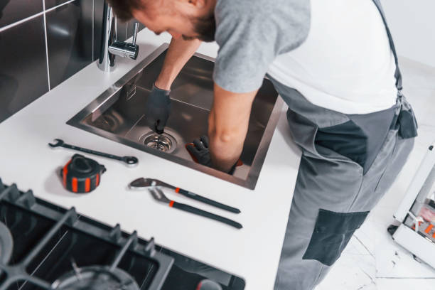 Young professional plumber in grey uniform working on the kitchen