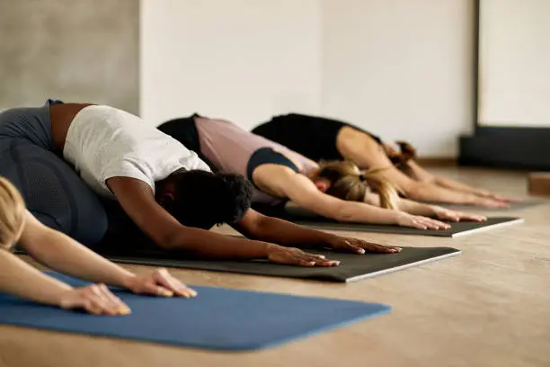 Group of female athletes warming up and stretching on the floor during Yoga class at health club. Focus is on black woman.
