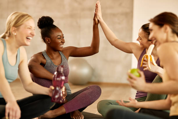 Happy athletic women giving high-five while relaxing after exercise class at health club. Group of cheerful sportswomen having fun on a break during sports training at health club. Two of them are giving high-five to each other. community health center stock pictures, royalty-free photos & images