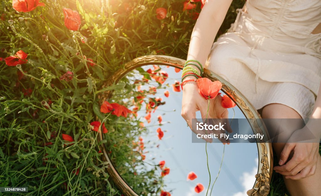 mirror reflection of sky, red poppies and woman hand holding flower. mirror reflection of sky, red poppies and woman hand holding flower. Summer beauty vibes background. Creative representation of summer time. accessory made of colored beads. Horizontal composition Mirror - Object Stock Photo