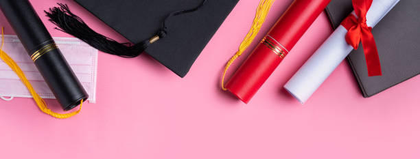 istock Graduation academic cap with diploma and mask isolated on pink table background. 1324878812