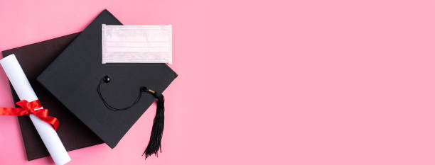 istock Graduation academic cap with diploma and mask isolated on pink table background. 1324878879