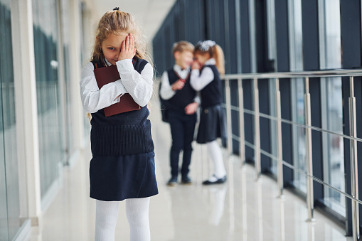 Little girl gets bullied. Conception of harassment. School kids in uniform together in corridor.