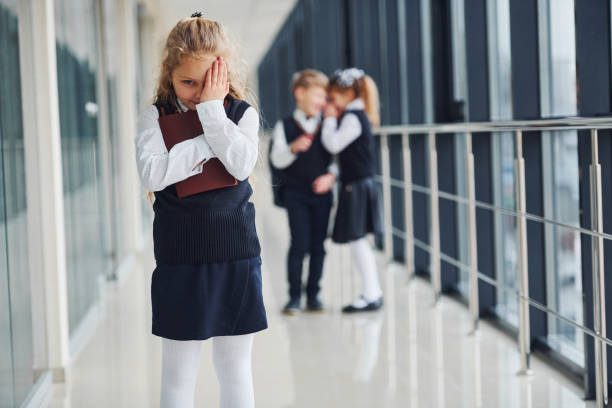 Little girl gets bullied. Conception of harassment. School kids in uniform together in corridor stock photo