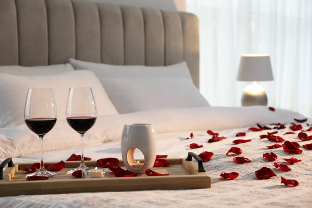 tablett mit gläsern rotwein, kerzen und rosenblättern auf dem bett im zimmer - romantic activity stock-fotos und bilder