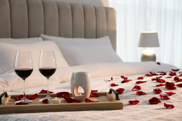 Tray with glasses of red wine, candles and rose petals on bed in room Tray with glasses of red wine, candles and rose petals on bed in room romantic activity stock pictures, royalty-free photos & images