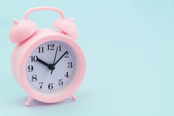 istock Pink alarm clock on blue background 1324884014