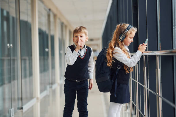 ein kleiner schuljunge stiehlt einem mädchen dinge aus der tasche, während sie musik hört - bullying child teasing little boys stock-fotos und bilder