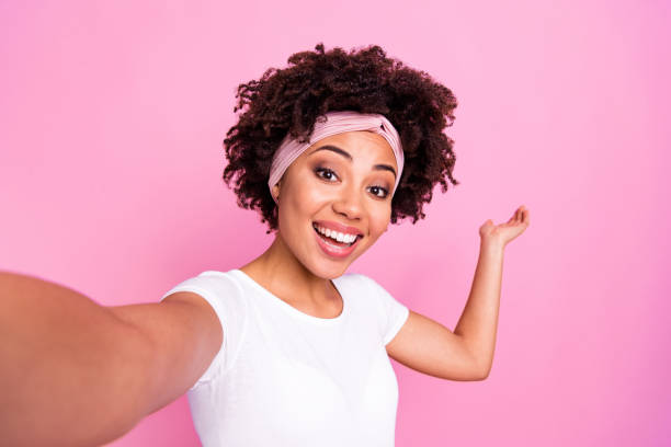 retrato fotográfico de una mujer bonita que muestra copyspace con la mano tomando selfie sonriendo aislado sobre fondo de color rosa pastel - autofoto fotos fotografías e imágenes de stock