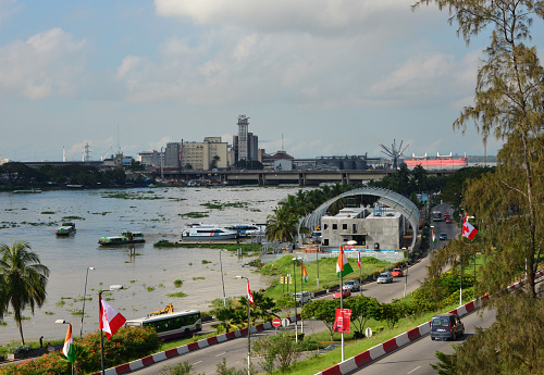 Abidjan, Ivory Coast / Côte d'Ivoire: Boulevard De Gaulle, the Plateau's waterfront avenue with the Aqualines Plateau boat station - in the background Houphouët-Boigny Bridge and the Grands Moulins d'Abidjan (GMA), industrial flour mill in Treichville, Petit Bassam island.