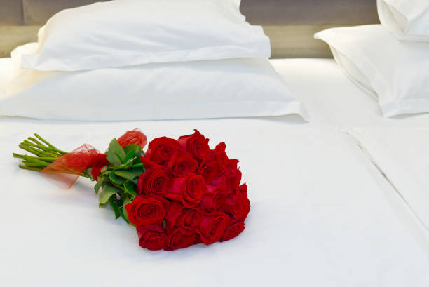 buquê de rosas vermelhas na cama em um quarto de hotel para lua de mel. encontro romântico de hóspedes no hotel. - honeymoon romance wedding bedroom - fotografias e filmes do acervo