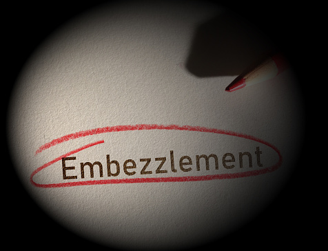 Embezzlement text circled in red pencil on a dark background