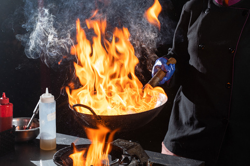 Flambe frying pan wok, cooking on fire. Pan-Asian cuisine. Street food