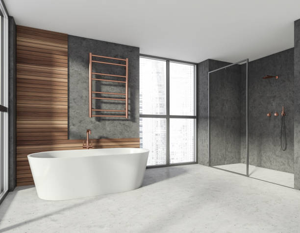 istock Modern stylish hotel bathroom interior, with ceramic bathtub, shower cabin. Grey wall, concrete floor. Panoramic window. City view. 1324892386