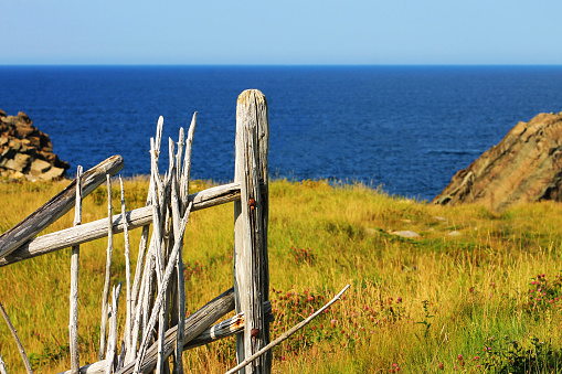 Close-up of a section of old, rustic, wood fence. View of hill and Atlantic ocean to the horizon, out of focus in the background.