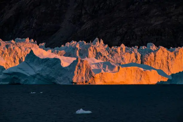 Late-afternoon sunlight strikes huge, rugged icebergs, painting them in warm orange colors, interrupted by shadowy areas of dark blue-green, Gaasefjord, King Christian X Land, Scoresbysund, Sermersooq, East Greenland, Greenland, Europe