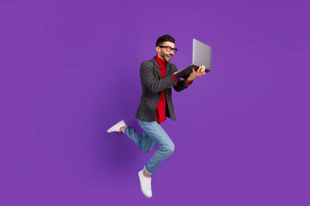 Full size profile photo of optimistic nice brown hair man jump with laptop wear spectacles sweater isolated on purple background Full size profile photo of optimistic nice brown hair man jump with laptop wear spectacles sweater isolated on purple background. high collar stock pictures, royalty-free photos & images