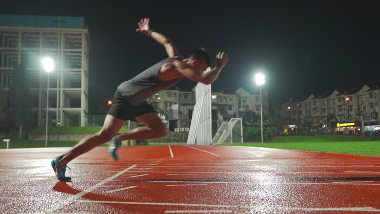 slow motion asian chinese male athlete running at men's track rainy late evening in stadium