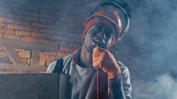 Black male builder in hardhat singing and playing level like guitar in smoke during break on construction site