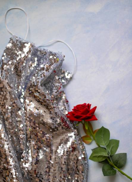 istock Shiny silver dress on a blue background next to an artificial rose. flat lay 1324896112