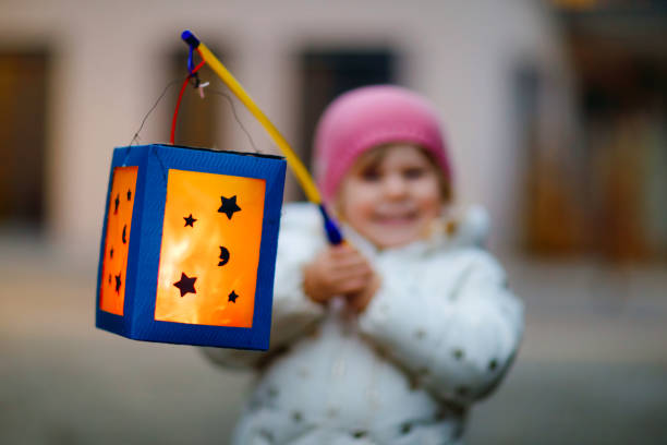 close-up of little kid girl holding selfmade lanterns with candle for st. martin procession. healthy toddler child happy about children and family parade in kindergarten. german tradition martinsumzug - optocht stockfoto's en -beelden