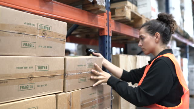 Female worker in uniform scanning boxes on warehouse rack
