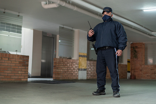 Latino man of average age of 50 years security guard of a building dressed in his blue uniform and his mask is inside the facilities with a radio in his hand