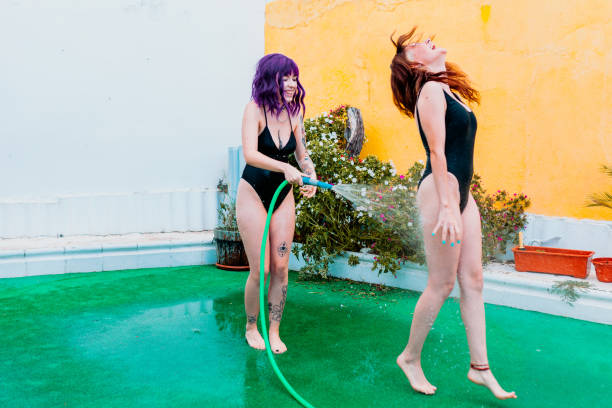 dos mujeres felices riendo en traje de baño jugando bajo gotas de agua de una manguera en el patio trasero - piel de gallina fotografías e imágenes de stock