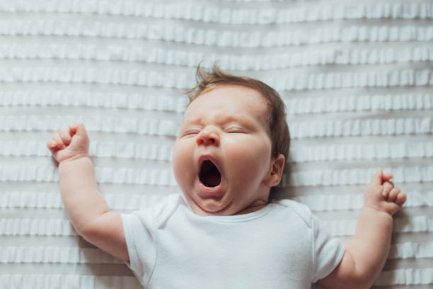 bébé qui dort et bâille sur des draps blancs - onesie photos et images de collection