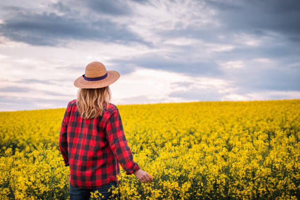 istock Woman with straw hat standing in oilseed rape field at spring 1324907962