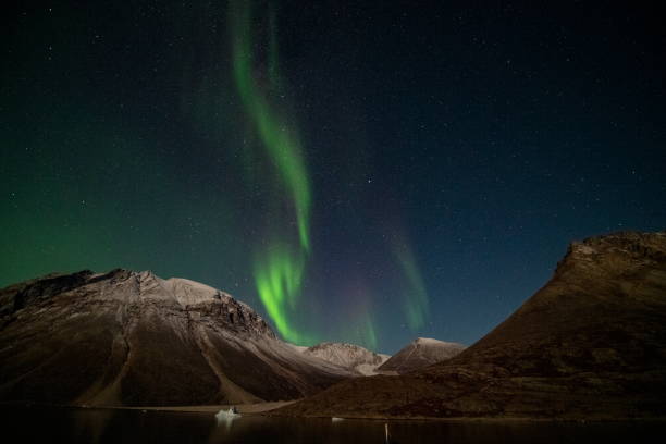Photo of The aurora borealis (northern lights) shows its colors in a protected bay on a calm night over a snow-dusted mountaintop